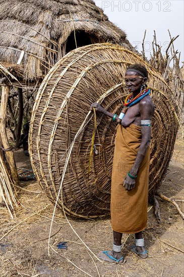 Woman before her hut with ready prepared reeds