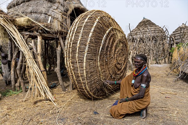 Woman before her hut with ready prepared reeds