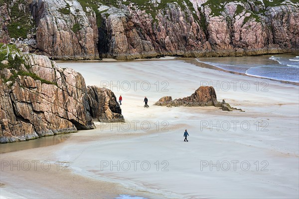 Walkers in bay with rocks and sandy beach