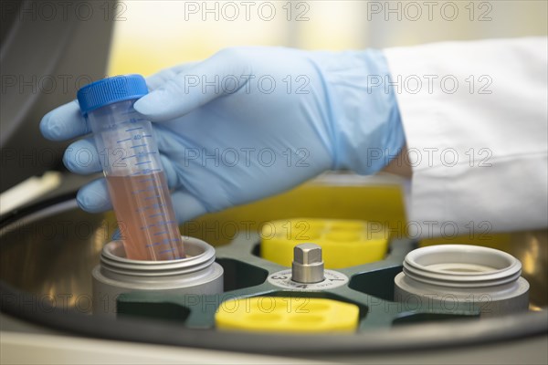 Hand of a medical laboratory assistant takes a centrifuge tube with liquid out of the centrifuge