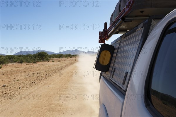 Looking back while driving a 4x4 on a gravel road with a dust cloud. Namibia