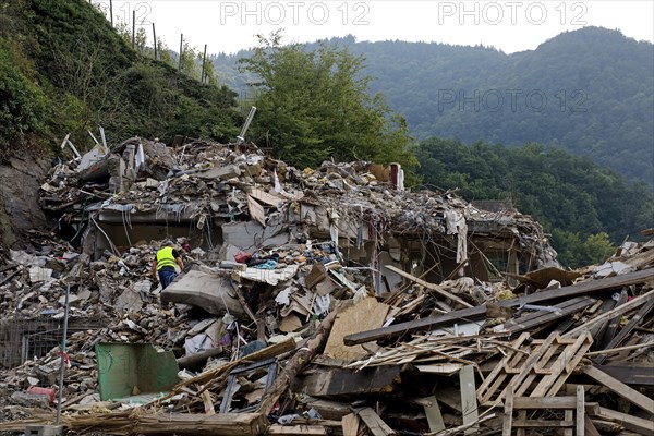 A man in mountains of rubble and rubbish in front of the Ahr mountains