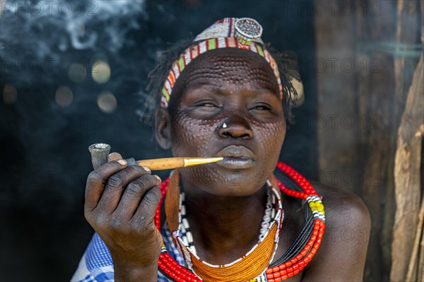 Woman with beauty scars from the Toposa tribe smoking a pipe