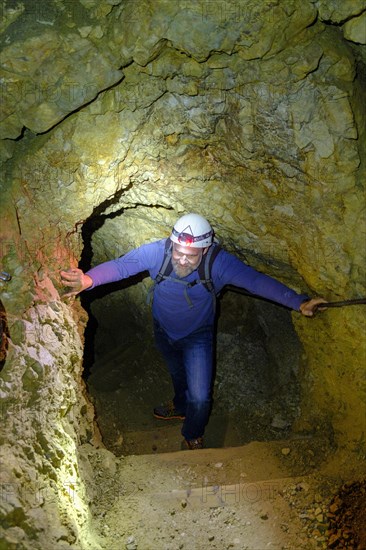 Climber with helmet and headlamp in rock tunnel