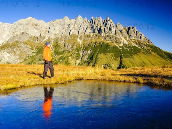 Mountaineer in front of mountain scenery reflected in a frozen mountain lake