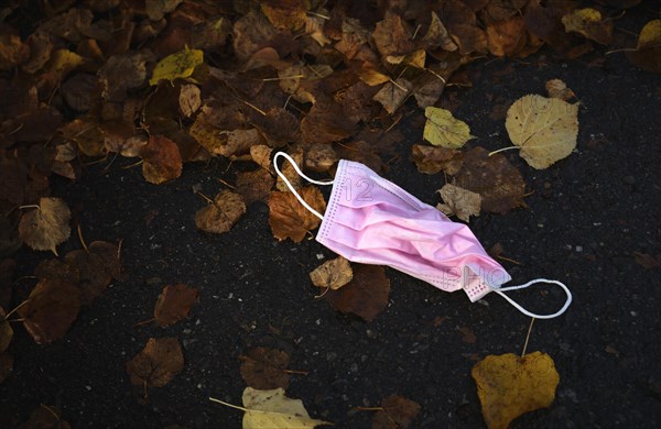 Discarded pink face mask lies on the ground in autumn leaves