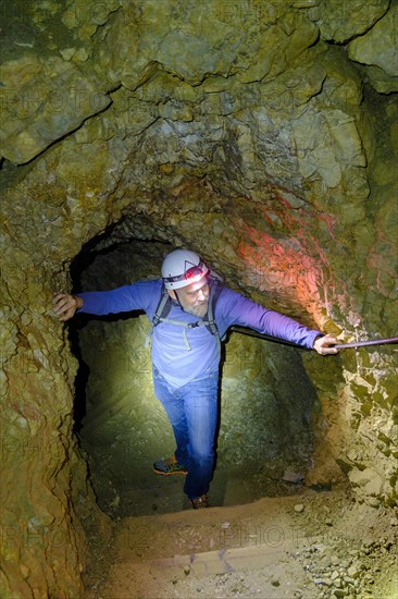 Climber with helmet and headlamp in rock tunnel