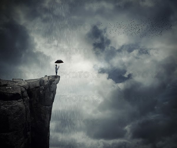 Man with an umbrella stand on the edge of the cliff