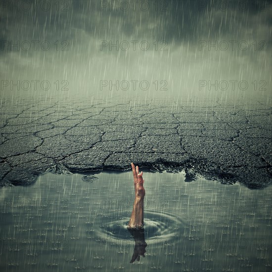 Surrealistic image with a single hand of drowning man asking for help in a pothole of cracked asphalt