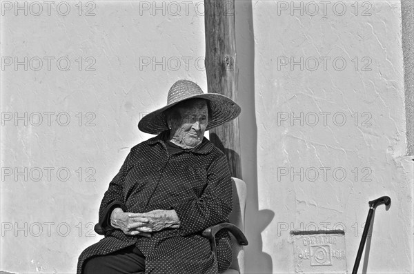 Old woman with folded hands sitting on chair with sun hat