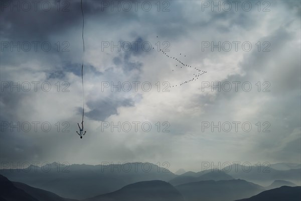 Young man falling from the sky with a rope tied to his leg as safety insurance