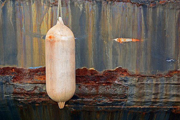 Pink fender in front of rusty ship's wall