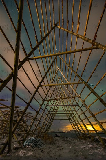 Aurora borealis over a worker in a wooden stockfish rack