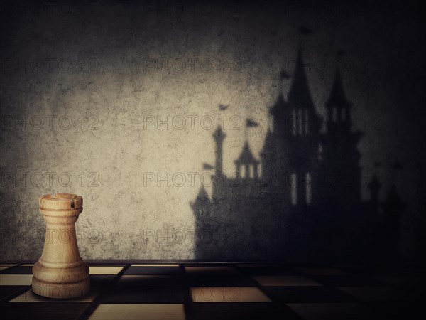 Rook chess piece casting a shadow in shape of a castle on a concrete wall