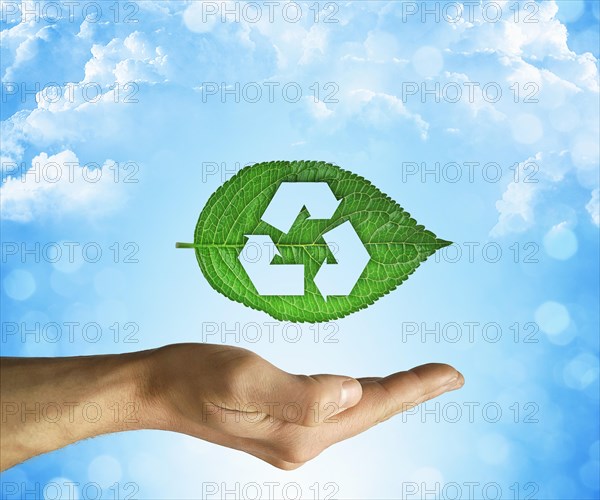 Opened hand holding a green leaf with recycling symbol on a blue sky background