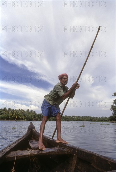 Boatman with a punt pole on a boat in the backwaters of Kerala