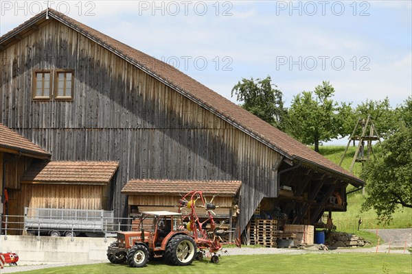 Fiat tractor with roundabout tedder in front of stable building