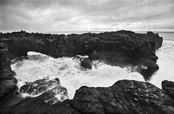 Lava arch on the volcanic coast at high tide with high waves