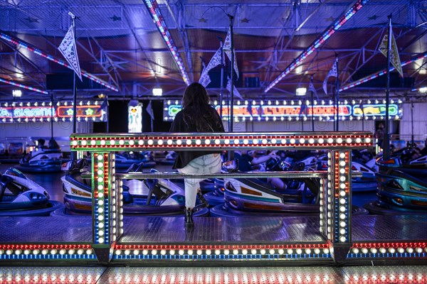 A back of a woman sitting by bumper cars at the late evening