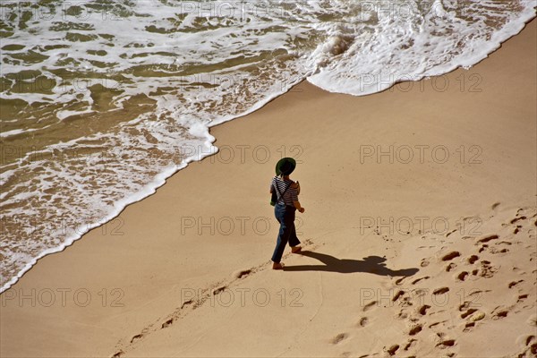 Clothed woman with hat walking on stand in front of wave fringe