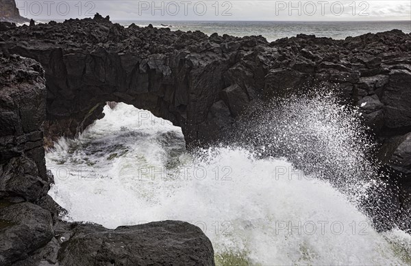 Lava arch on the volcanic coast at high tide with high waves