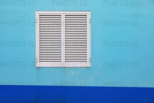 Light blue house facade with closed white shutters