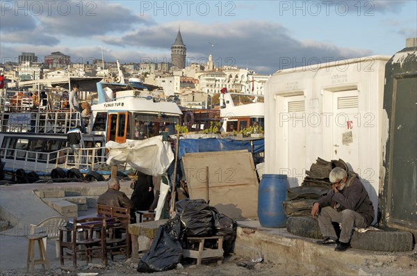 Man sitting on old car tires in Eminoenue harbor district with view of Galata Tower