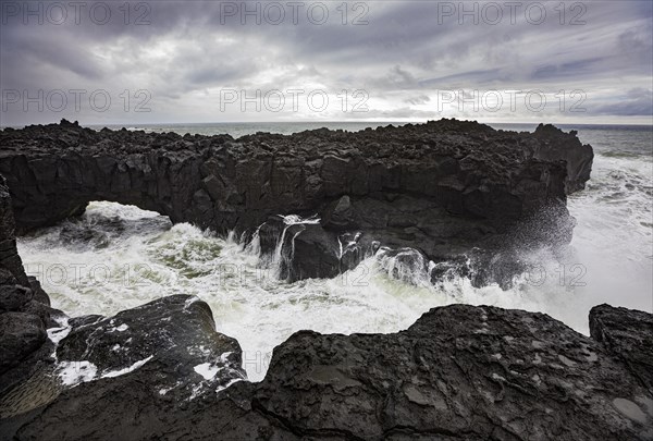 Lava arch on the volcanic coast at high tide with high waves