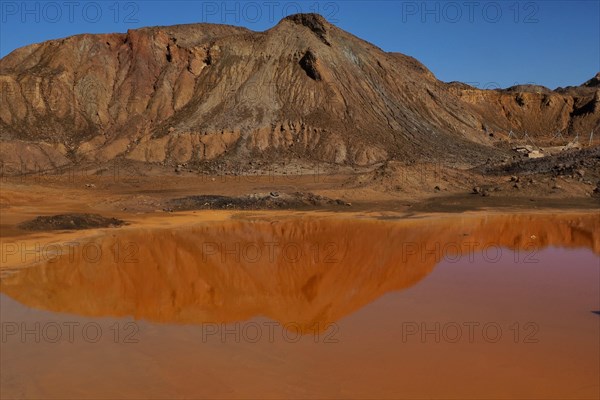 Mountain reflected in red puddle on mine site