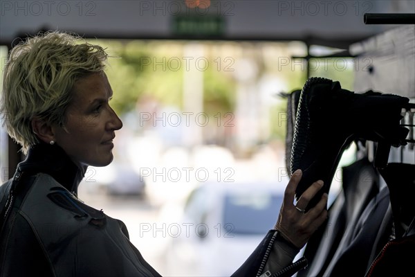 Blond woman in wetsuit choosing boots for water adventure