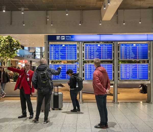 Passengers and staff stand in front of the blue screens for departure times at Frankfurt Airport