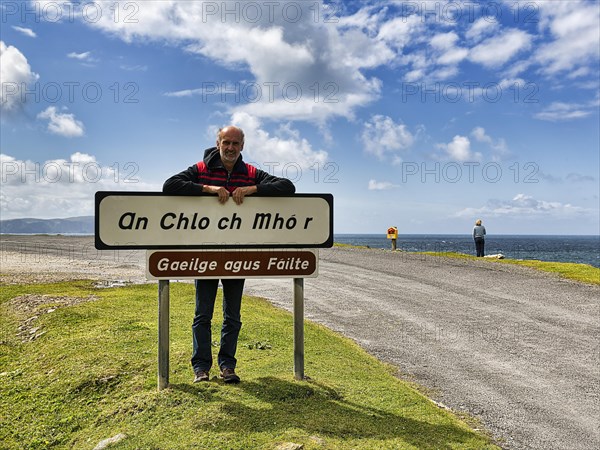 Tourist leaning against welcome sign in Irish