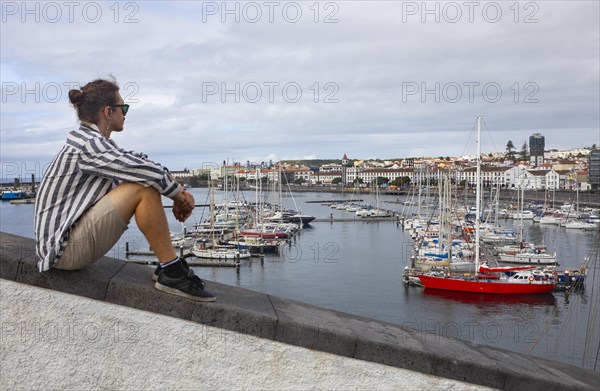 Young man sitting on the promenade in the marina of Ponta Delgada