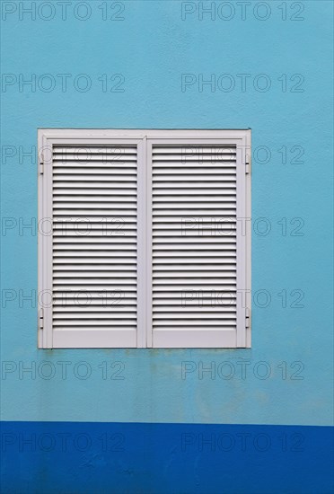 Light blue house facade with closed white shutters