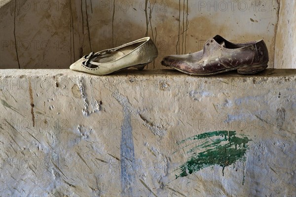 Lady's shoe with man's shoe on wall in front of wall with traces of rain