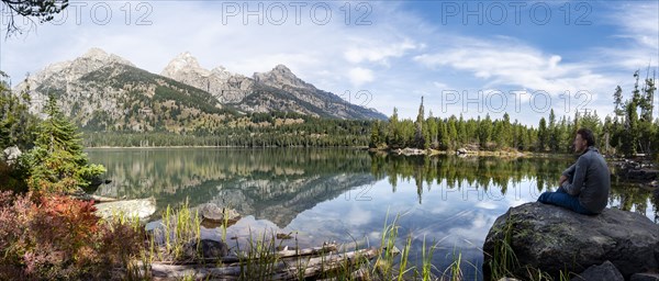 Young man sitting on a stone by a lake