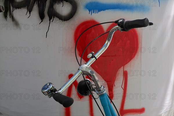 Handlebars from bicycle in front of wall with red heart symbol