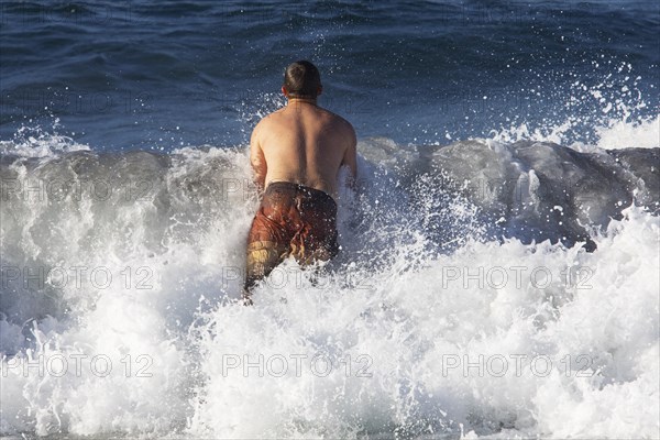 Young man jumps into a high wave on the beach of Praia de Santa Barbara