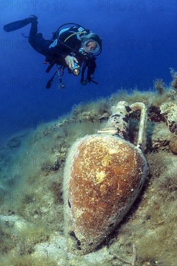 Diver looking at and illuminating ancient amphora on seabed