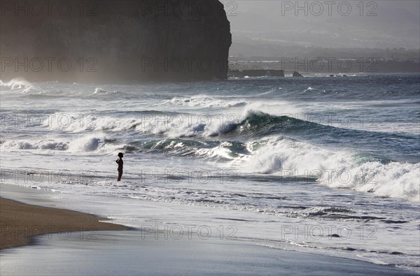 A woman standing on the sandy beach of Praia de Santa Barbara in stormy sea with high waves