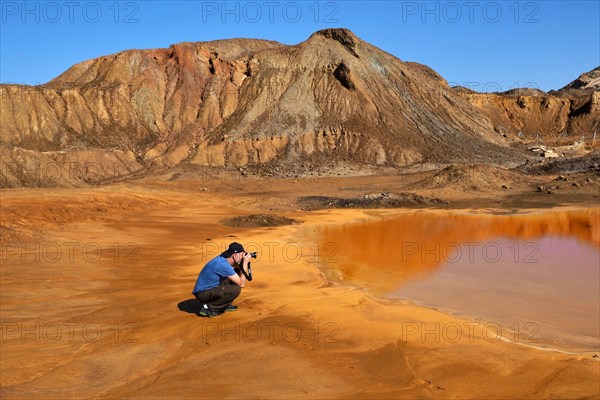 Photographer in front of mountain with red puddle on mine site