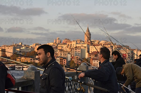 Anglers at the Golden Horn on Galata Bridge with view the Galata Tower at sunset