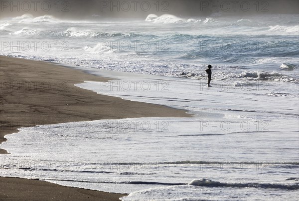 A woman standing on the sandy beach of Praia de Santa Barbara in stormy sea with high waves