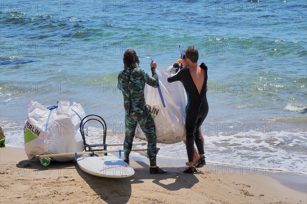 Two men in diving suits hoist heavy bag of plastic waste onto a transport board