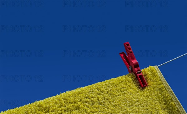 Yellow towel with red clothes peg on clothesline in front of blue sky