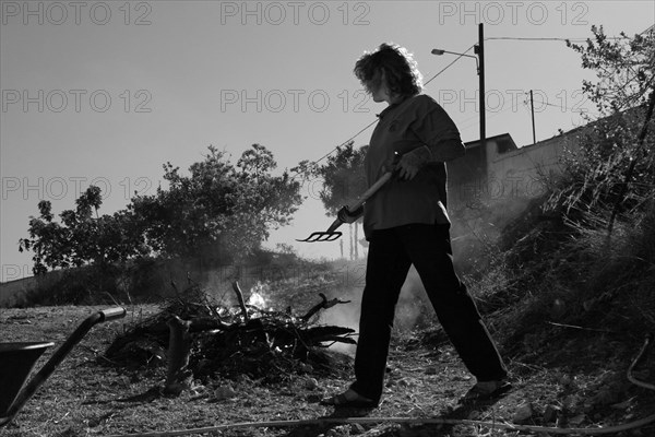 Woman with pitchfork in front of fire with garden waste