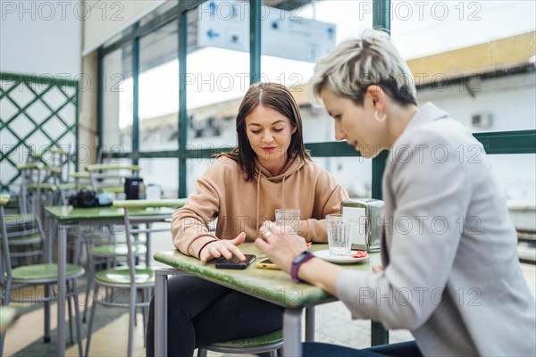 Two women chatting and showing something on the phone in the cafe at train station