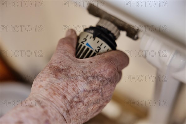 Hand of a senior citizen with age spots on the thermostat of a heater