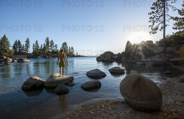 Young man in swimming trunks standing on a round stone in the water