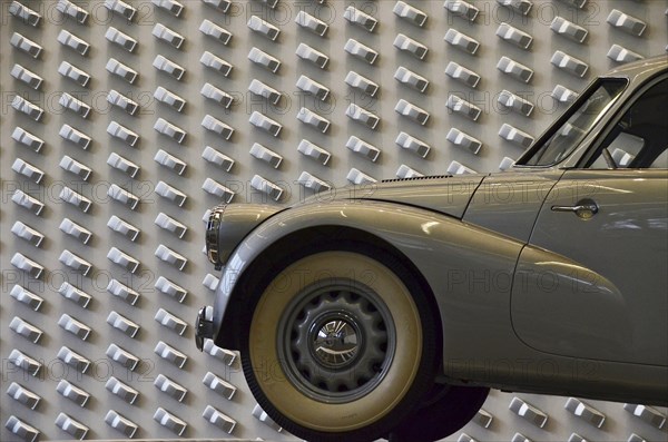 Grey vintage car with whitewall tyres in front of Audi design wall